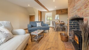 A cozy living room with a fireplace, a sofa, a coffee table, and a dining area with a table and chairs. - Willow Cottage (South Creake) (2), South Creake, Norfolk (South Creake)