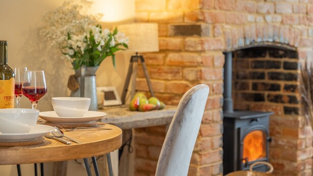 A cozy dining area with a brick fireplace, a wooden table set with plates, bowls, and wine glasses. - Willow Cottage (South Creake) (2), South Creake, Norfolk (South Creake)