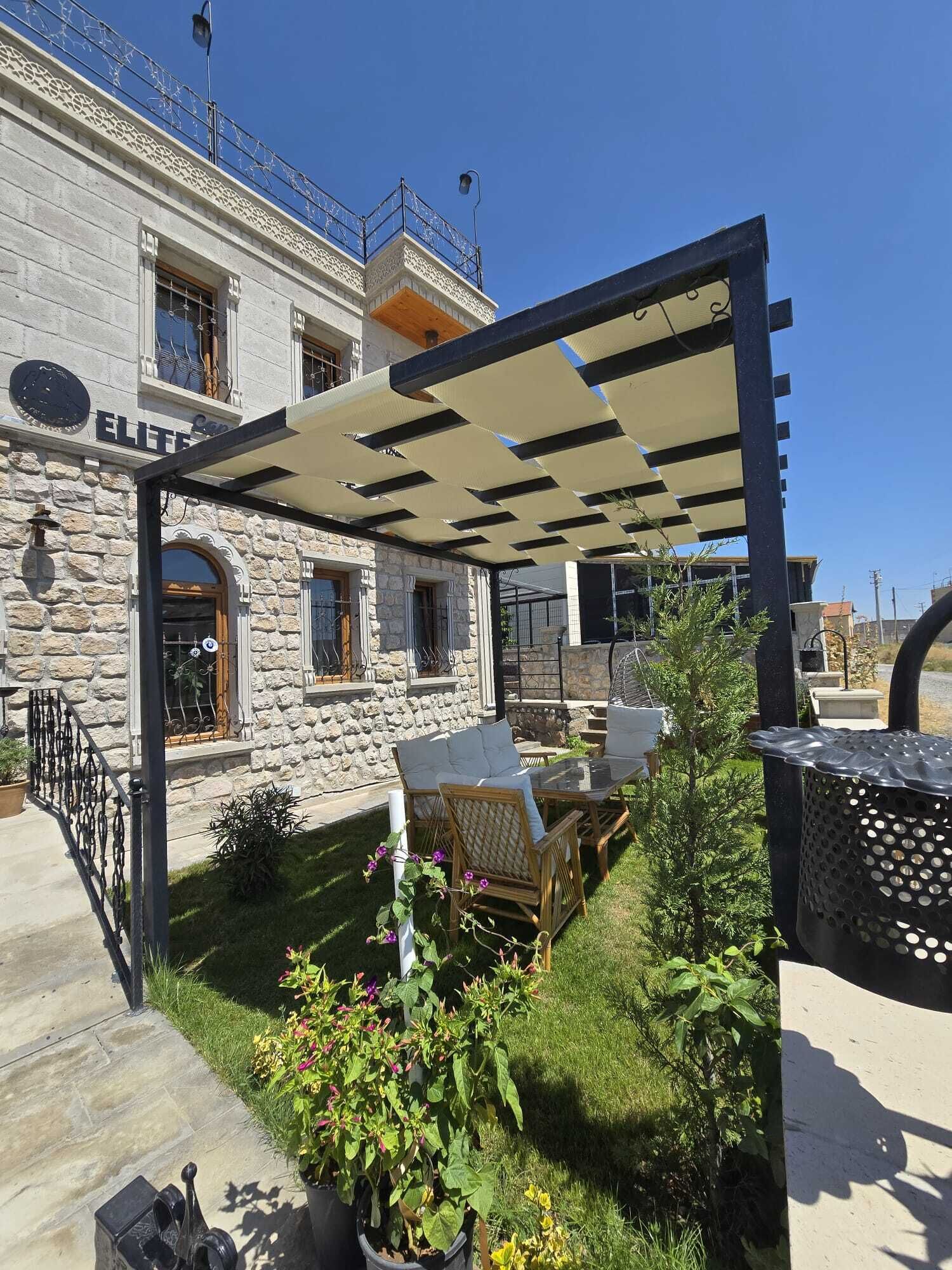 A stone building with a covered outdoor seating area, a small garden, and a metal fence.