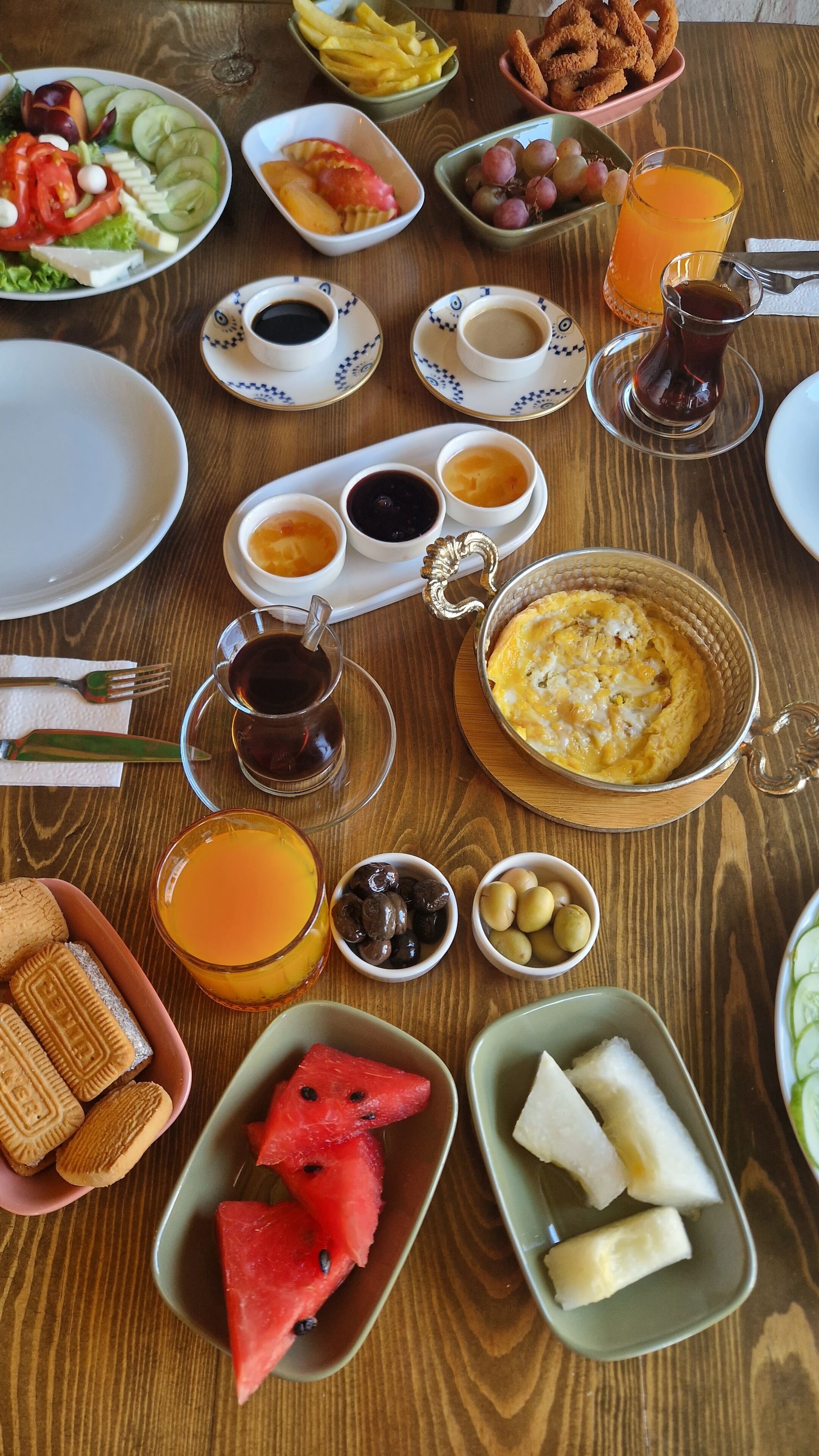 A wooden table with various breakfast items including fruits, pastries, and beverages.