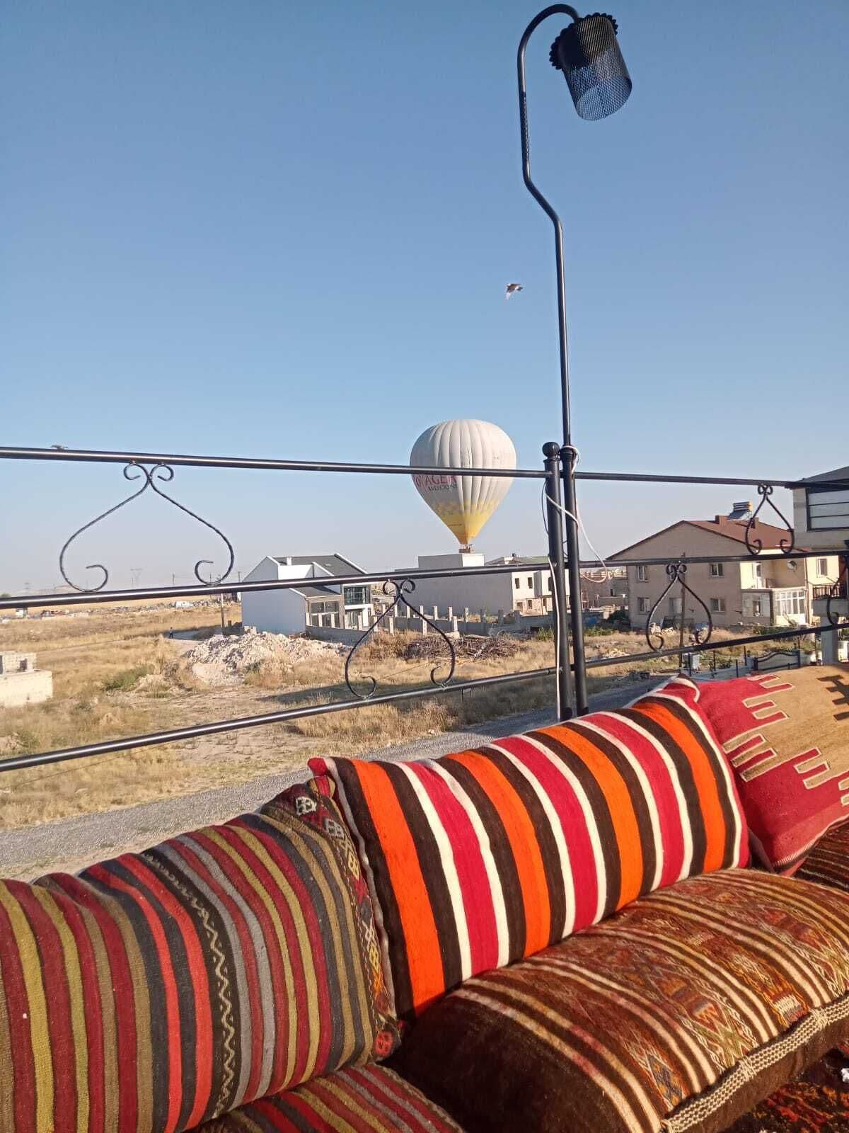 Un balcón con un sofá a rayas, una lámpara colgante y un globo aerostático al fondo.