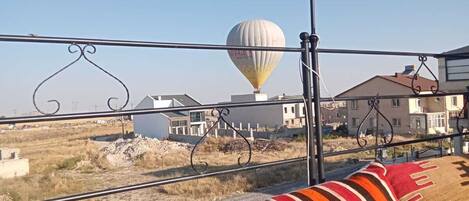 Un balcón con un sofá a rayas, una lámpara colgante y un globo aerostático al fondo.