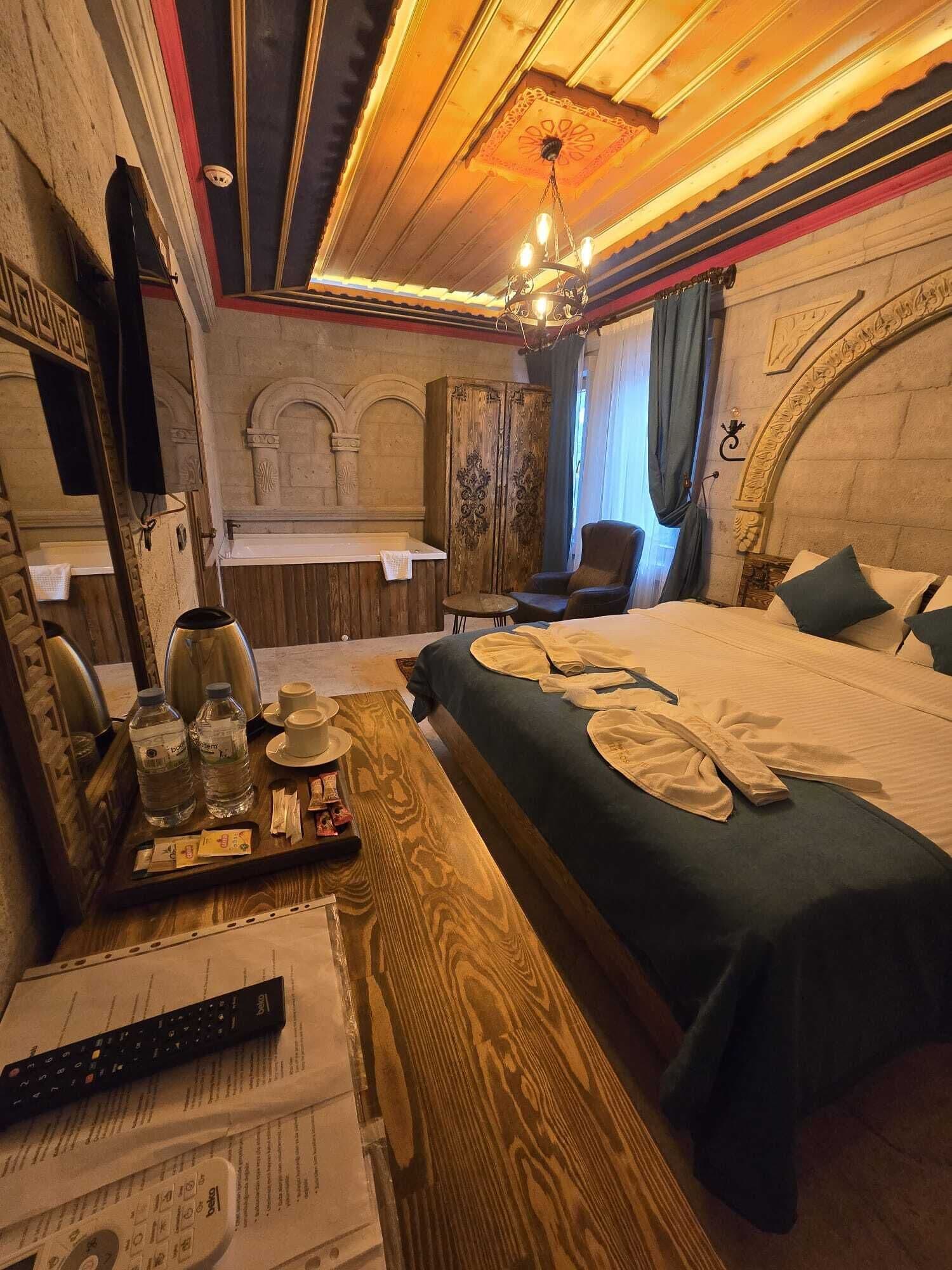 Habitación de hotel con techo de madera, una cama grande, cómoda de madera, una silla y tocador con espejo.