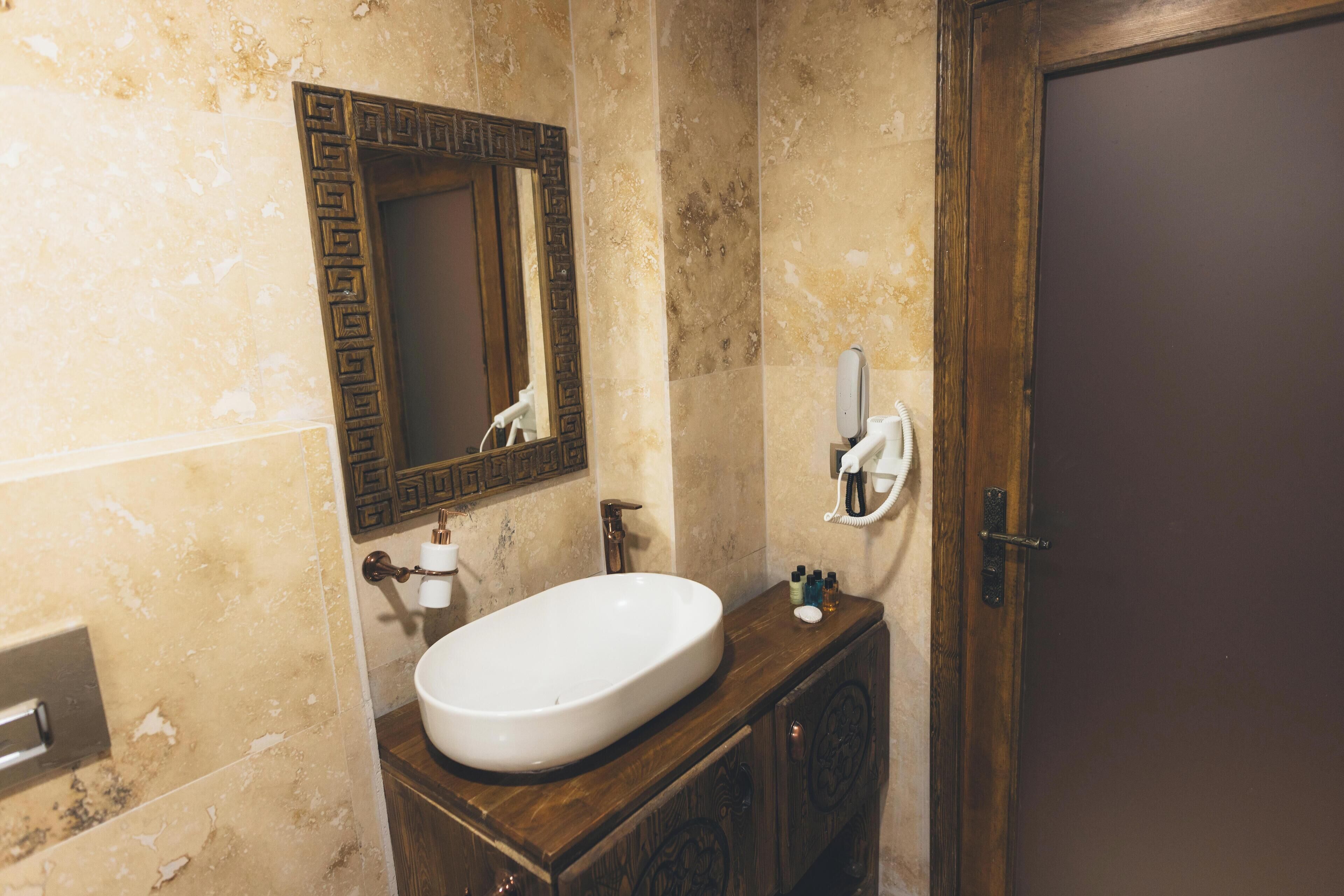 A bathroom with a white sink, a mirror with a decorative frame, a towel dispenser, and a wooden cabinet.