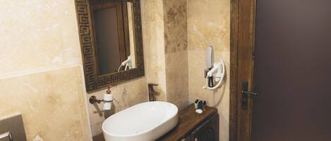 A bathroom with a white sink, a mirror with a decorative frame, a towel dispenser, and a wooden cabinet.