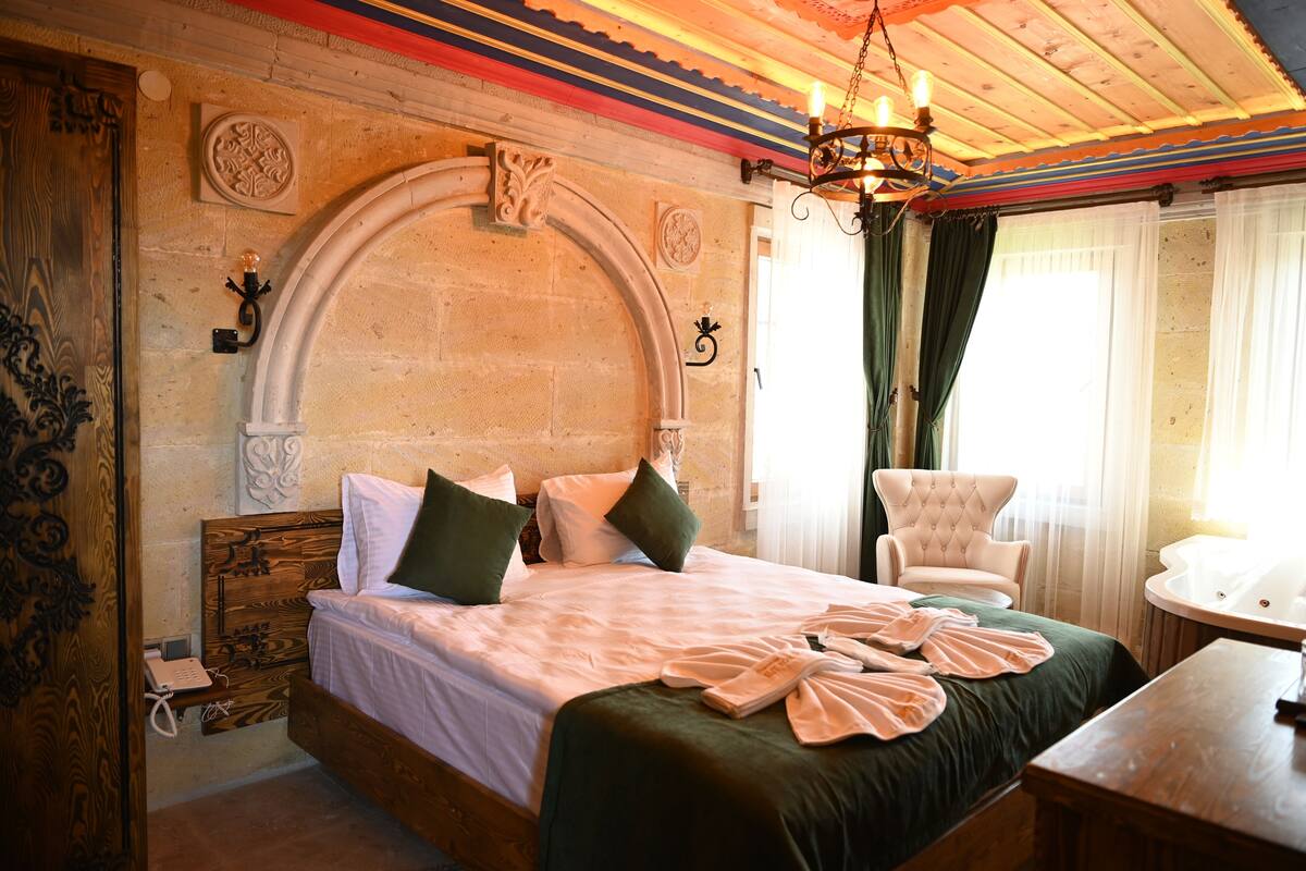 A hotel room with a large bed, a chair, a small table, and a bathroom with a bathtub.