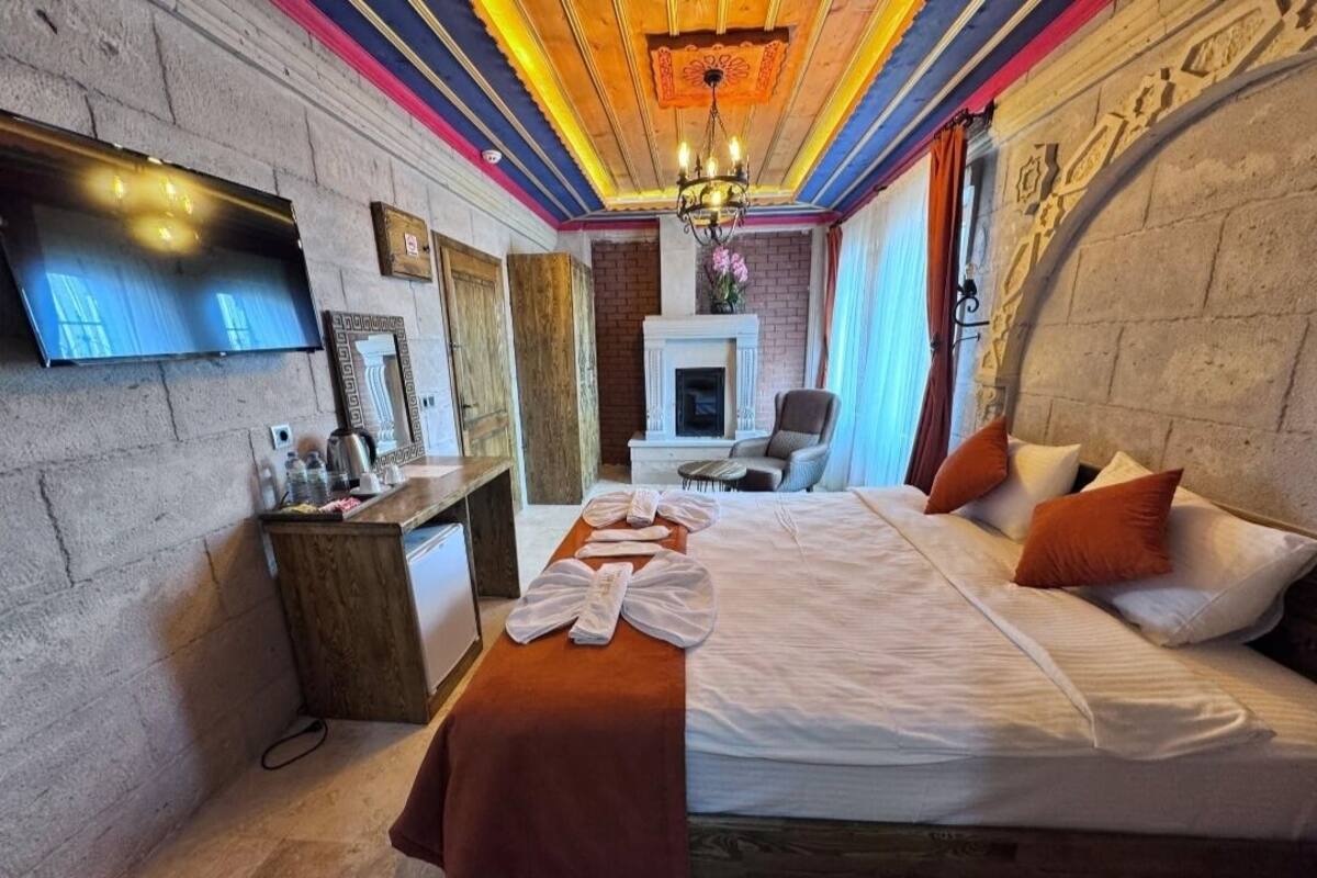 A hotel room with a bed, a desk, a TV, and a fireplace.