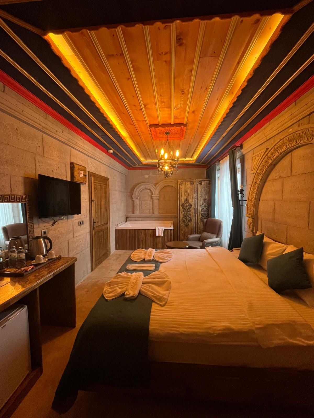 Habitación de hotel con una cama grande, un escritorio con televisor de pantalla plana, un área de descanso con una silla y una pared de piedra.