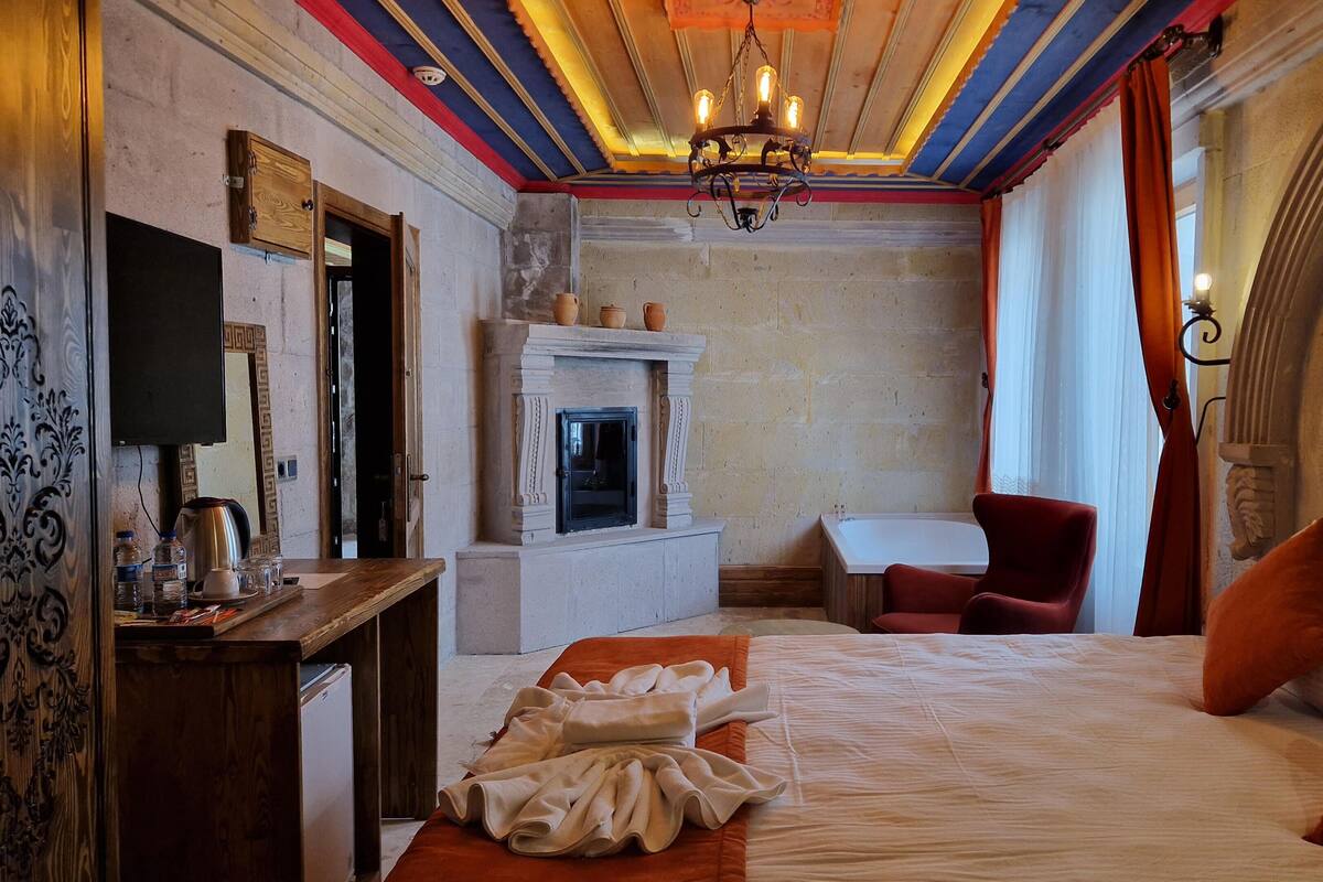 A hotel room with a bed, a desk with a chair, a fireplace, and a television.
