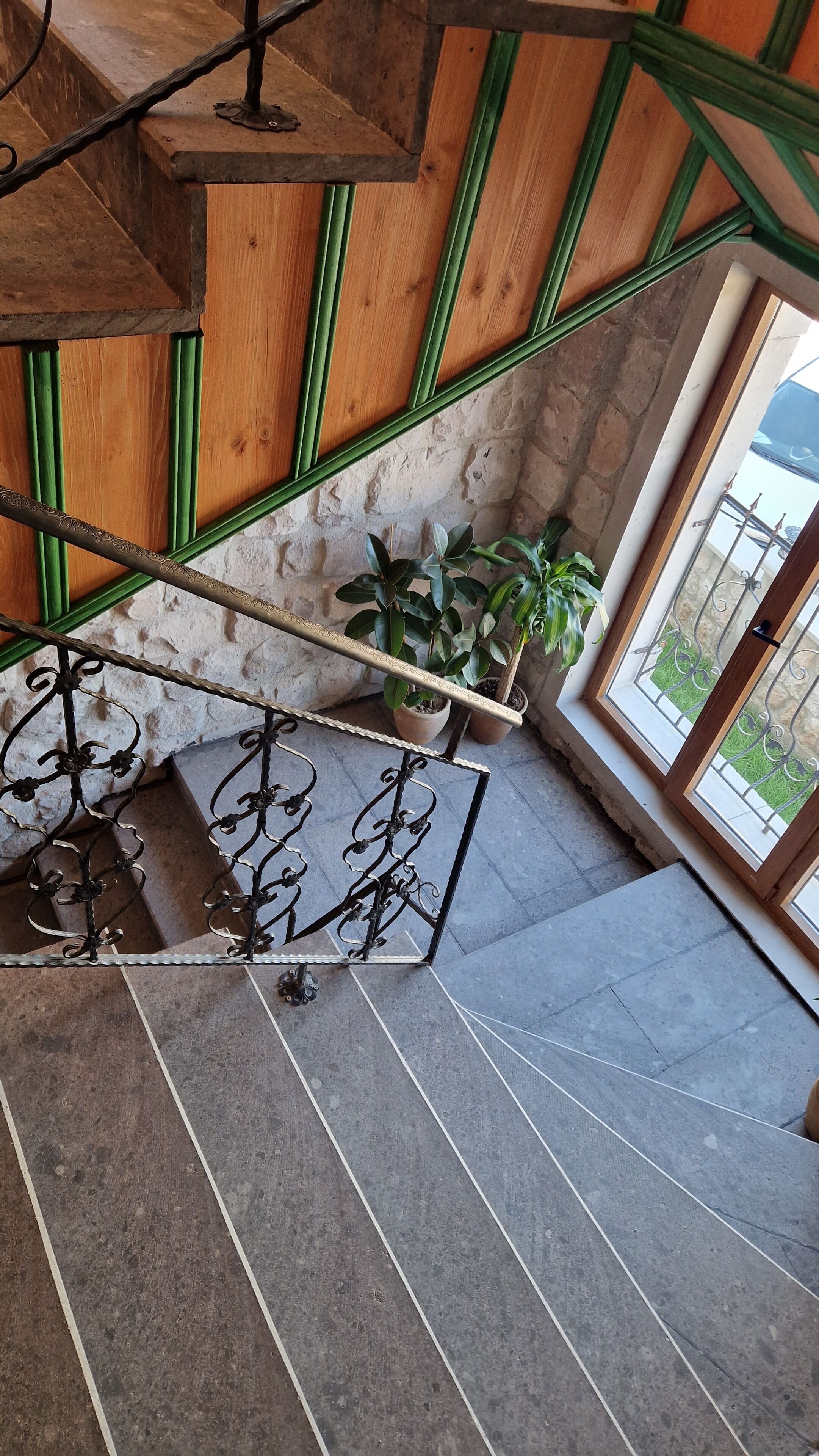 Een trap met groen geschilderde leuningen en een metalen handrail, leidend naar een kamer met een stenen muur en uitzicht op het landschap.