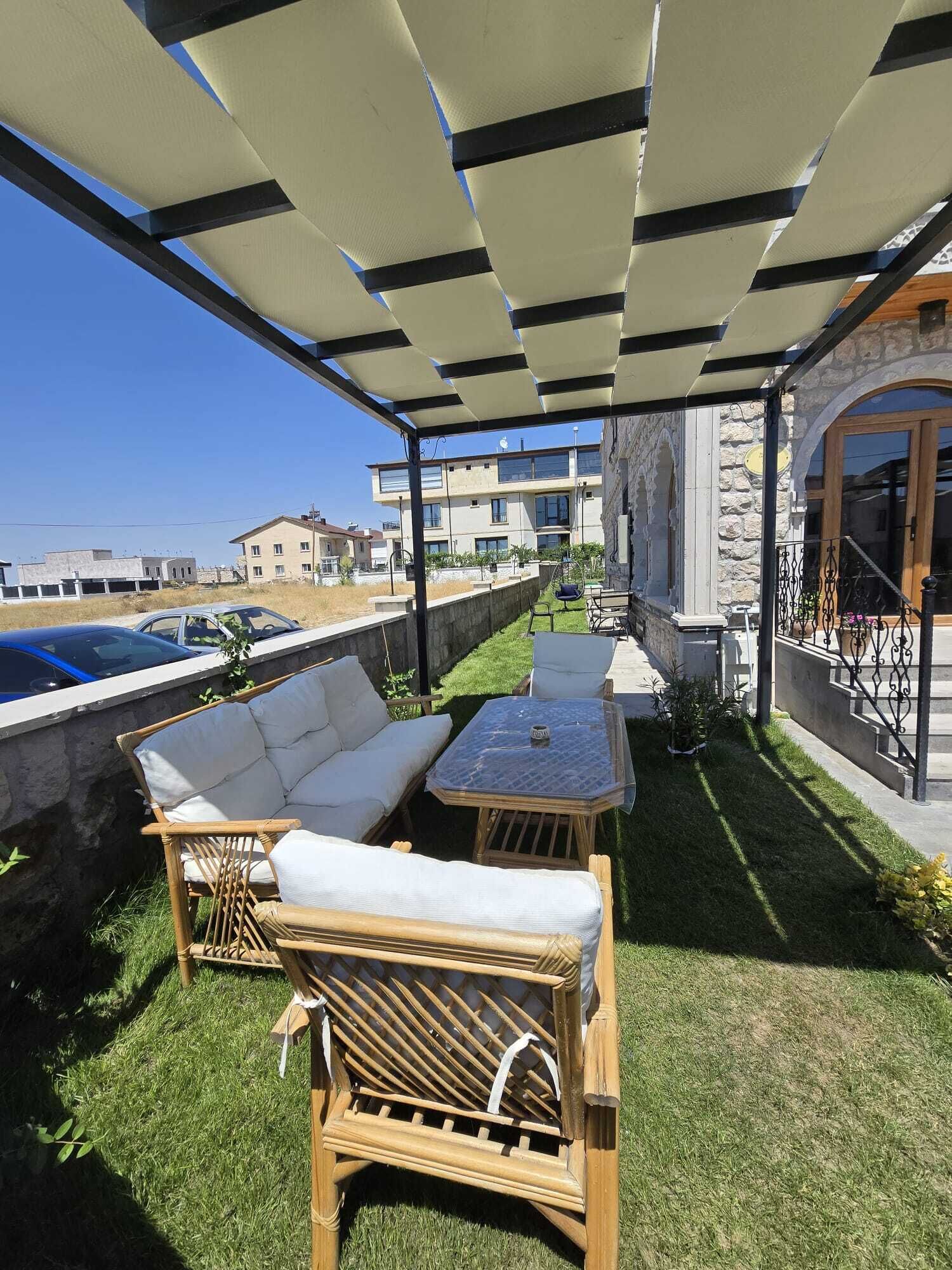 A covered outdoor seating area with a sofa and table, a stone wall, and a view of buildings in the background.