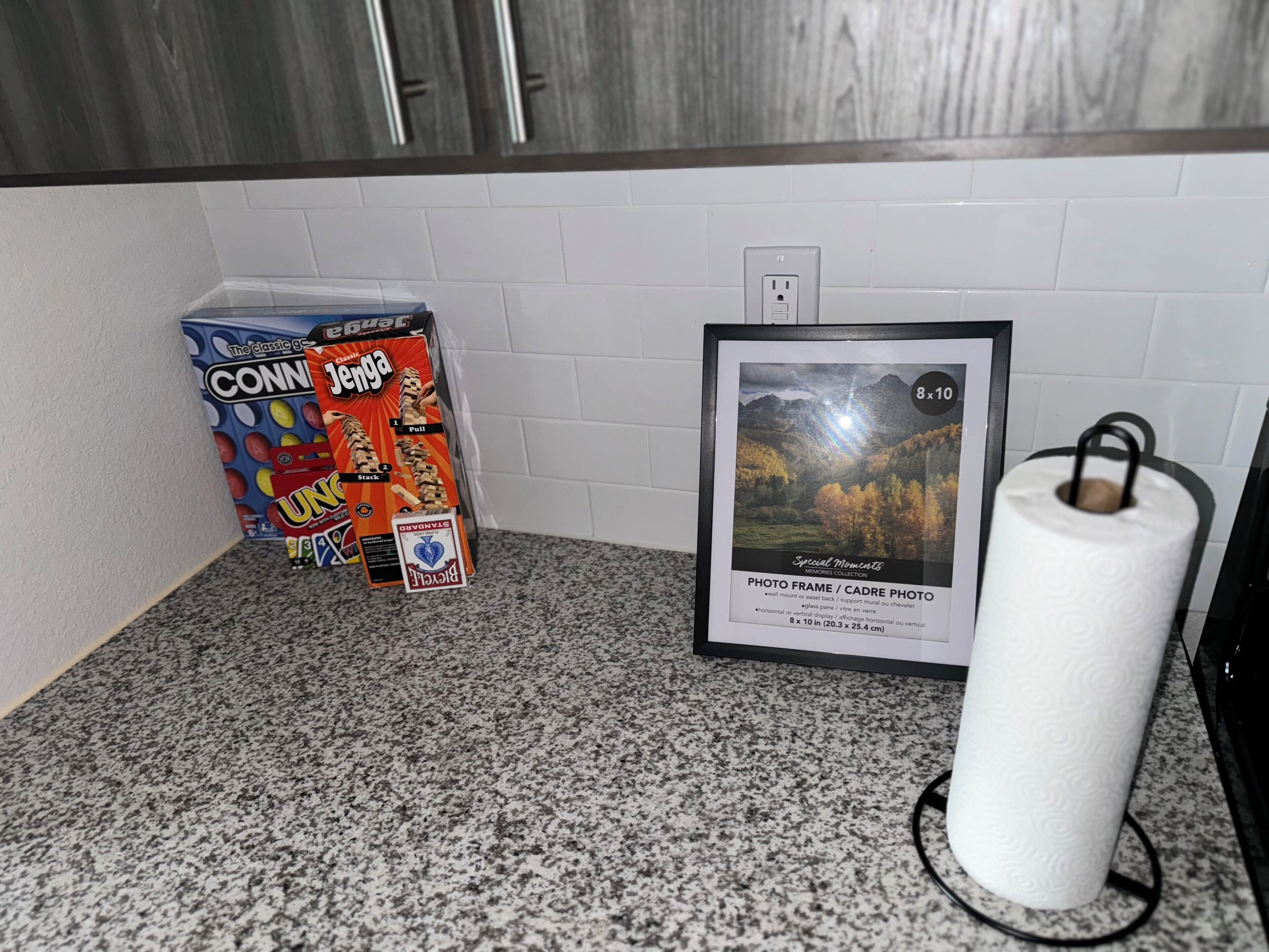 Una encimera de cocina con una foto enmarcada, un rollo de toallas de papel y una caja de Jenga.