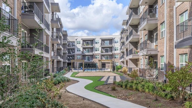A modern apartment complex with multiple balconies, a central courtyard with a curved pathway, and a building entrance. - Your Cozy & Captivating Condo! (Houston)
