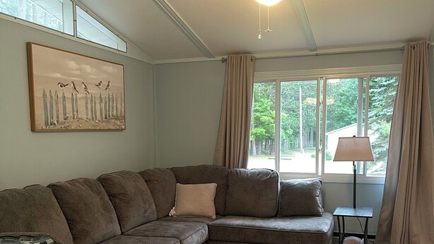 A living room with a sectional sofa, a ceiling fan, a lamp, and a window with curtains.