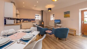 A modern kitchen with white cabinets, a microwave, and a wood-burning stove. - Two bedroom barn conversion on Anglesey | Bwthyn-Cerrig (Llannerch-y-medd)