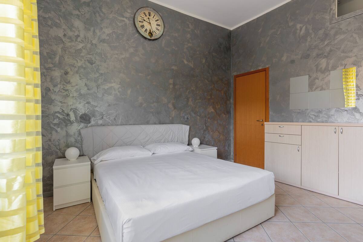 Ein Schlafzimmer mit einem Bett, Nachttischen, einer Uhr, einem Kleiderschrank und einem Spiegel.