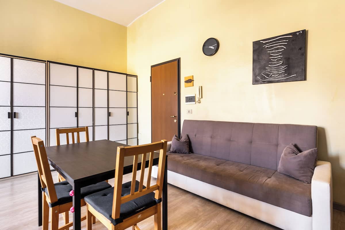 Ein Zimmer mit Esstisch, Stühlen, einer Couch, einer Uhr und einem gerahmten Kunstwerk an der Wand.