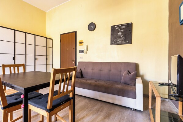 A living room with a sofa, a dining table with chairs, a TV, and a clock on the wall. - Gramsci 3 Studios by Wonderful Italy (Bologna)