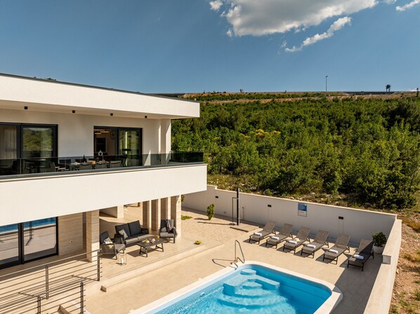 Um hotel moderno com piscina no terraço, área de estar ao ar livre e vista para uma encosta arborizada.