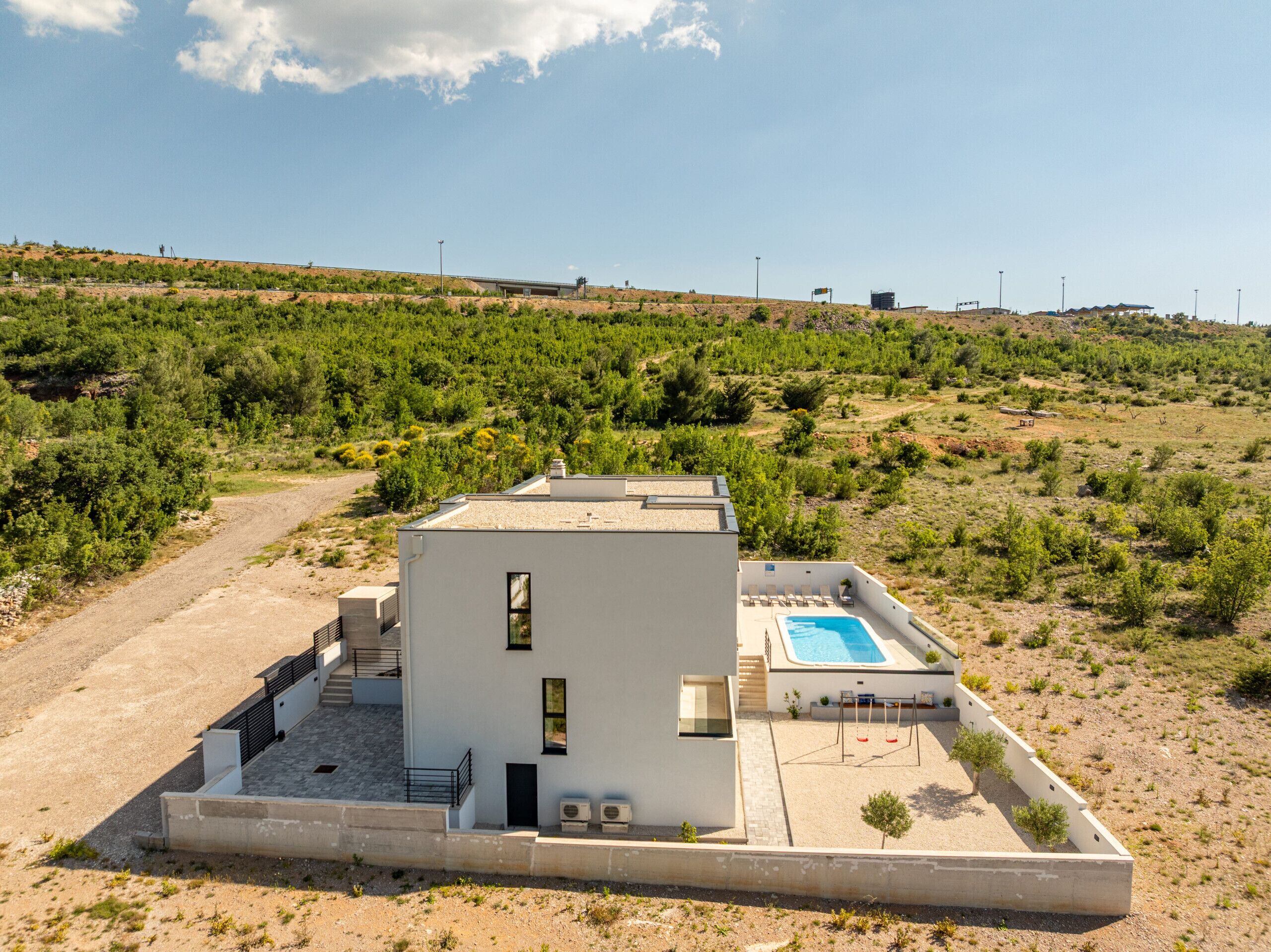 Un bâtiment moderne doté d’une piscine, entouré d’un paysage aride et vallonné.