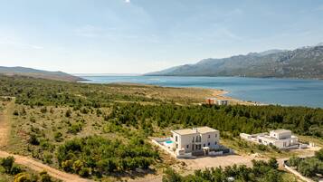Ein Küstenanwesen mit moderner Architektur, einem Swimmingpool und Blick auf Meer und Berge.