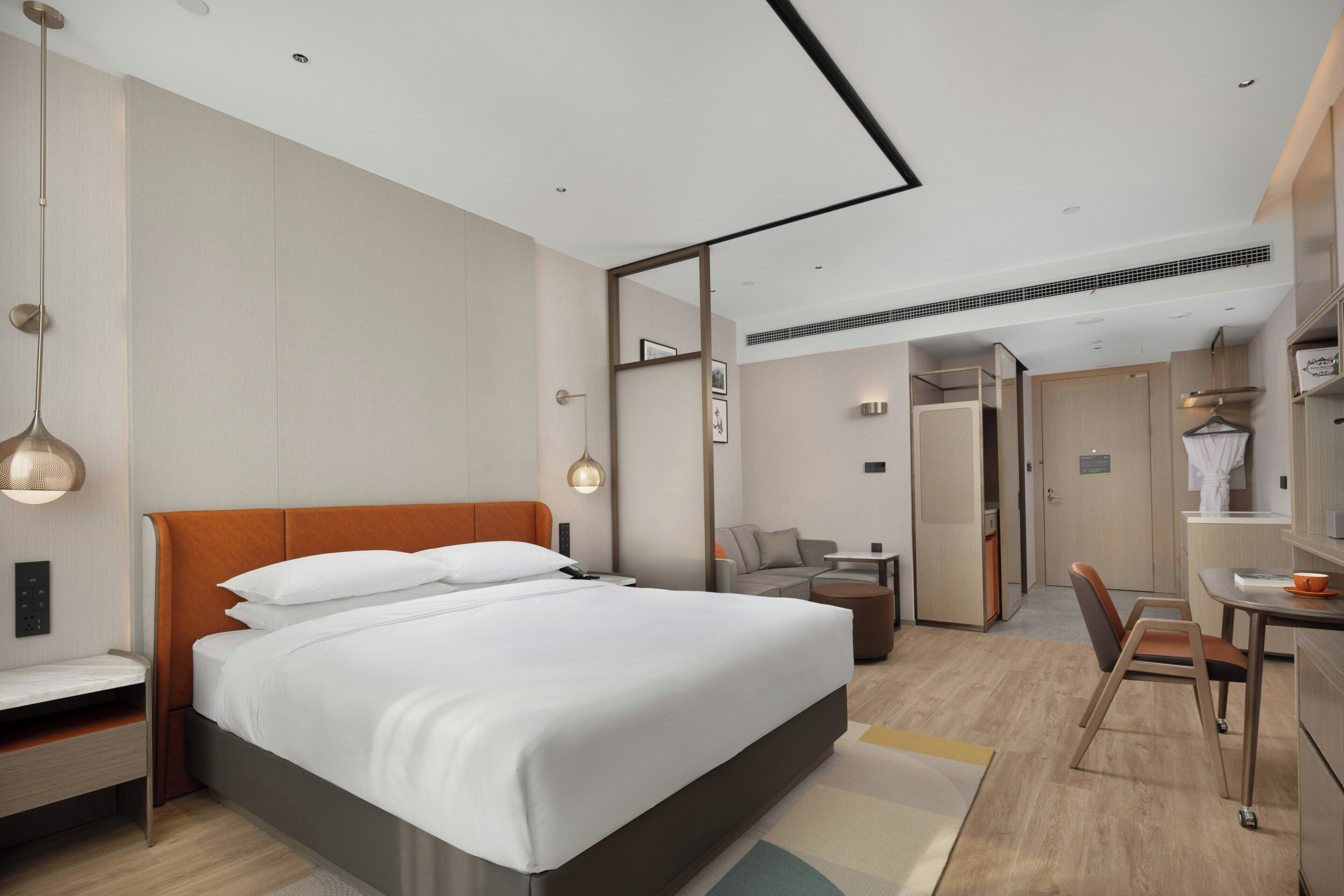 A modern hotel room with a large bed, a desk, a chair, and a wardrobe.