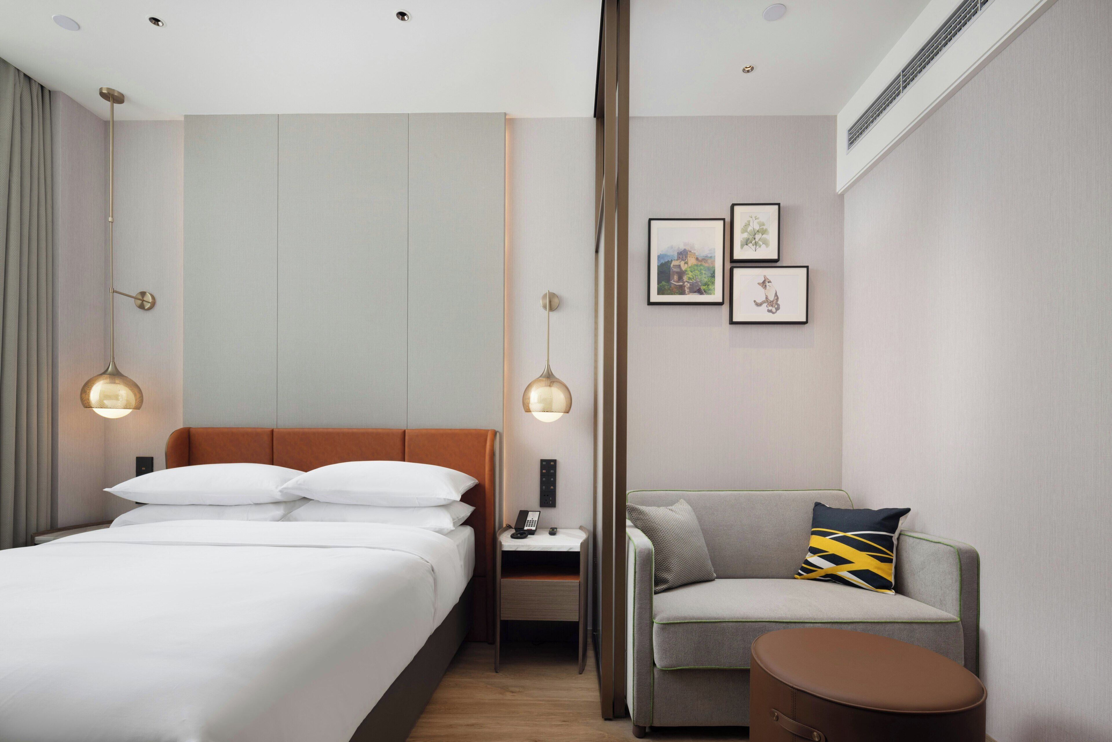 A hotel room with a bed, bedside table, lamp, chair, and artwork on the wall.