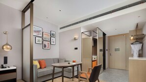 Une chambre d’hôtel moderne, équipée d’un canapé, d’une table, d’une chaise, d’un bureau, d’une lampe et de tableaux encadrés accrochés au mur.