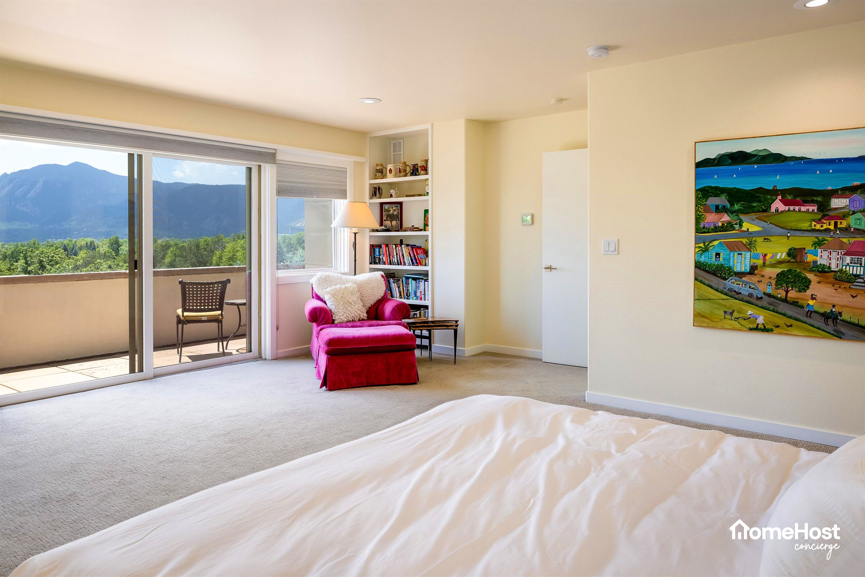 A hotel room with a large bed, a red armchair, a bookshelf, and a painting on the wall.