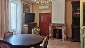 Un coin repas comprenant une table ronde, des chaises, un lustre, un téléviseur, une cheminée et un meuble en bois.
