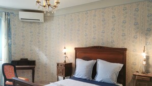 Une chambre avec un lit en bois, un bureau et une chaise. Il y a un climatiseur mural et un lustre.