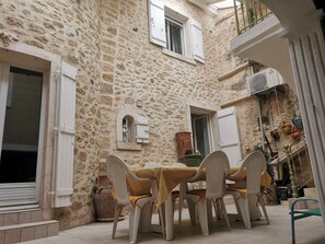 A stone building with a courtyard featuring a table and chairs, a window, and a door. - LA Maison DE Choubaka (Alignan-du-Vent)