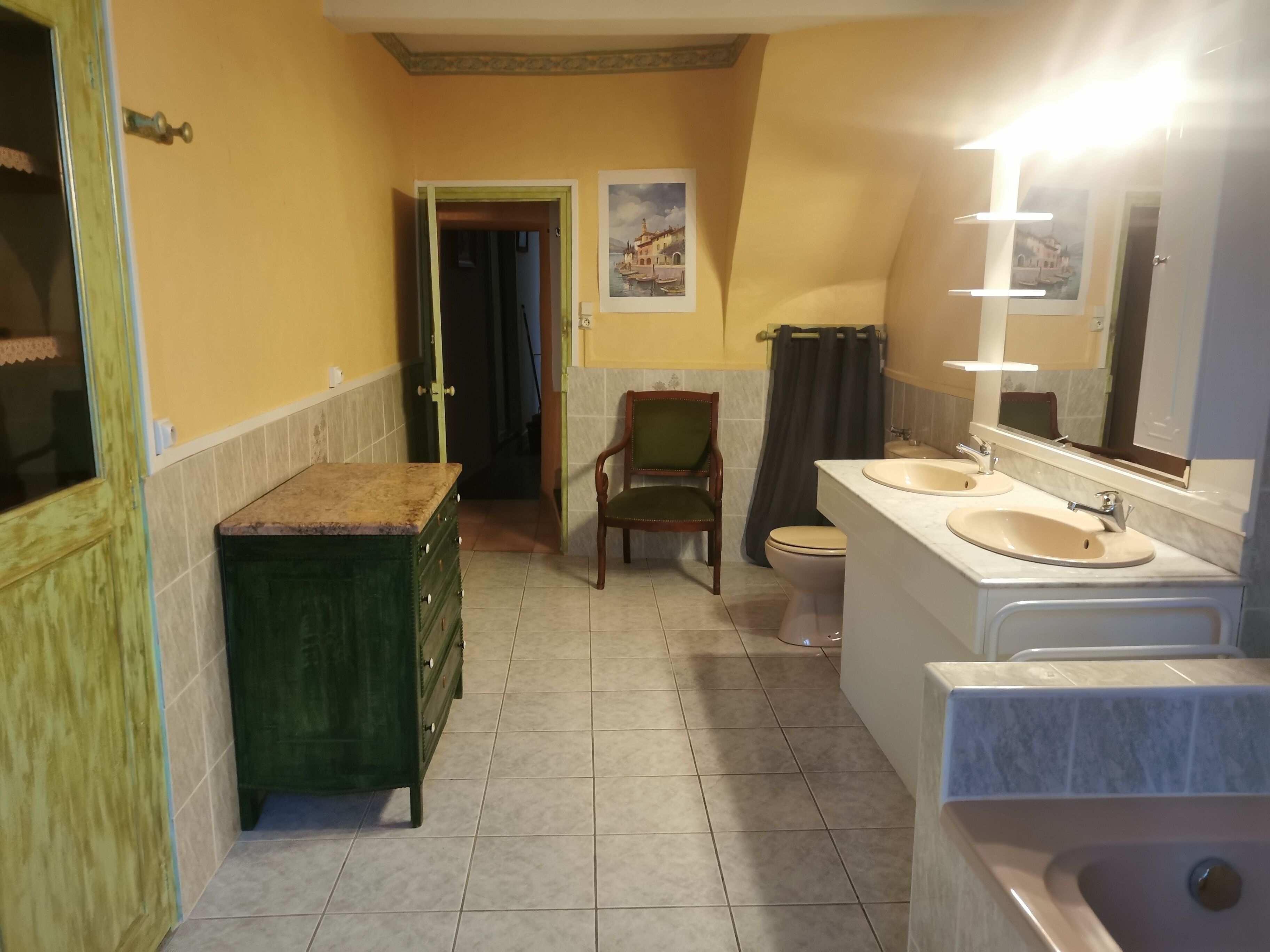 A bathroom with two sinks, a toilet, a chair, and a cabinet.