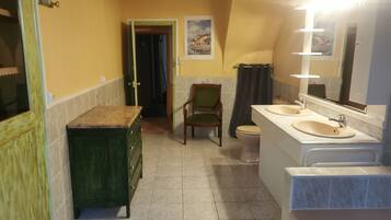 A bathroom with two sinks, a toilet, a chair, and a cabinet.