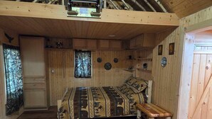 A wooden cabin interior with a bed, a bench, a door, and a window with a forest view. - Cozy cabin in Brasher Falls, NY (Brasher Falls)