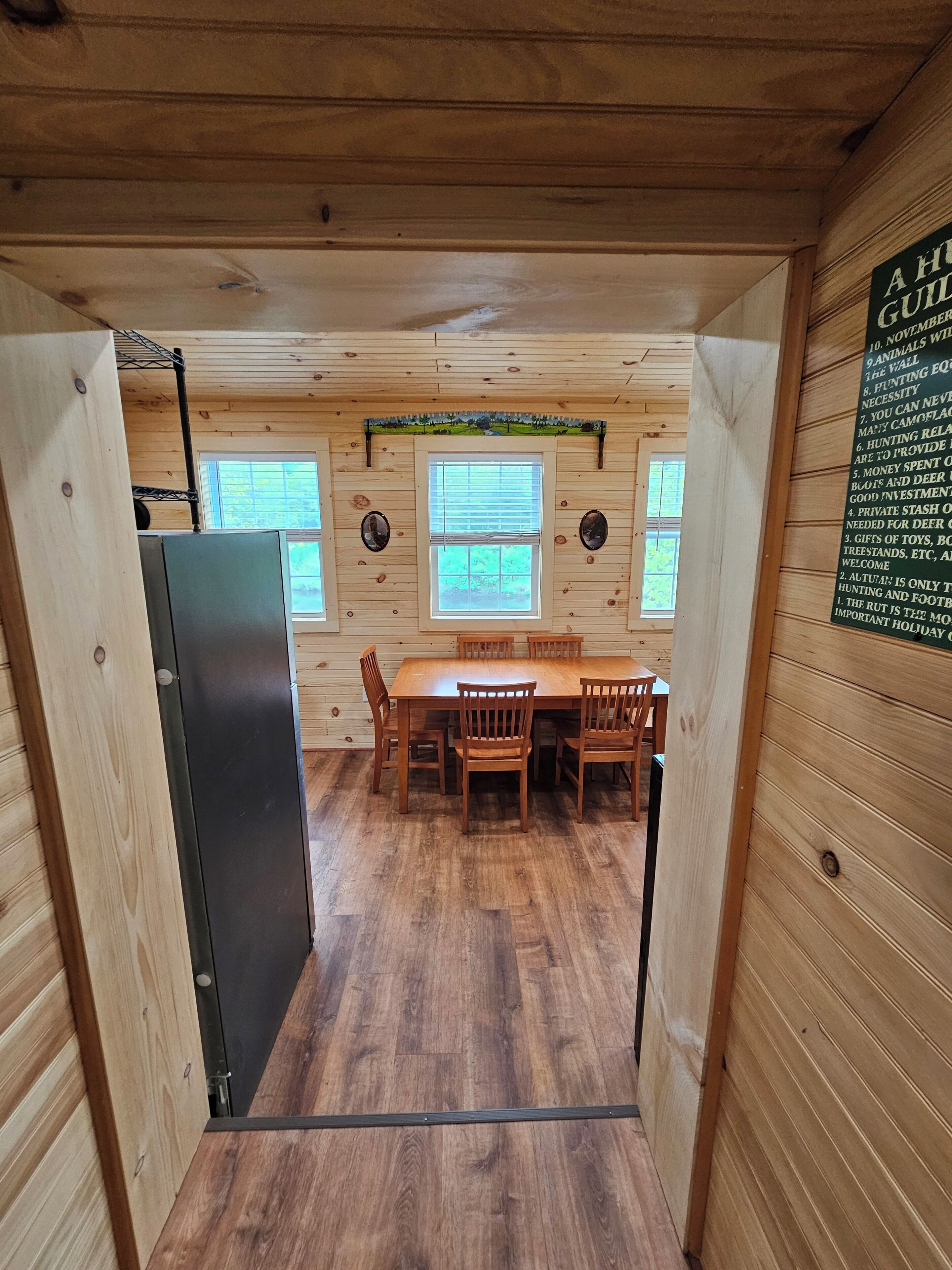 Ein Holzblockhaus-Innenraum mit Esstisch und Stühlen, einem Kühlschrank und einer Pinnwand an der Wand.