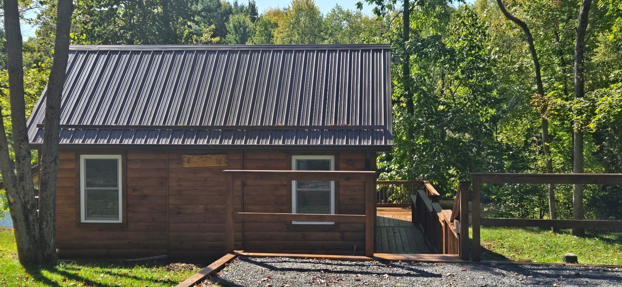 A wooden cabin with a metal roof, a wooden deck, and a gravel driveway.