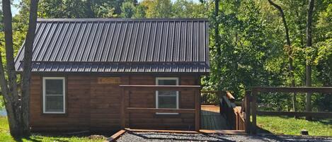 A wooden cabin with a metal roof, a wooden deck, and a gravel driveway.
