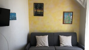 Un sofá gris con dos almohadones, un televisor montado en la pared y dos cuadros enmarcados.