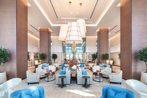 A spacious lobby with modern seating, a central decorative plant arrangement, and a large chandelier. - Waterfront 2BR Apartment in The Address Fujairah Residences Block C, Fujairah (Fujairah)