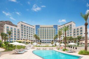 A hotel with a swimming pool, palm trees, and a mountainous backdrop.