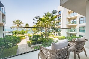 A balcony with wicker chairs and a view of a landscaped garden and buildings.