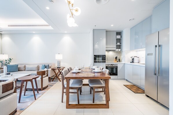A modern kitchen with a dining area, featuring a wooden table and chairs, a built-in oven, and a refrigerator. - Waterfront 2BR Apartment in The Address Fujairah Residences Block C, Fujairah (Fujairah)