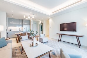 A modern living room with a dining area, a kitchen in the background, and a flat-screen TV mounted on the wall. - Waterfront 2BR Apartment in The Address Fujairah Residences Block C, Fujairah (Fujairah)
