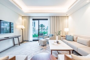 A modern hotel room with a large flat-screen TV, a sofa, a coffee table, and a view of palm trees through the window.