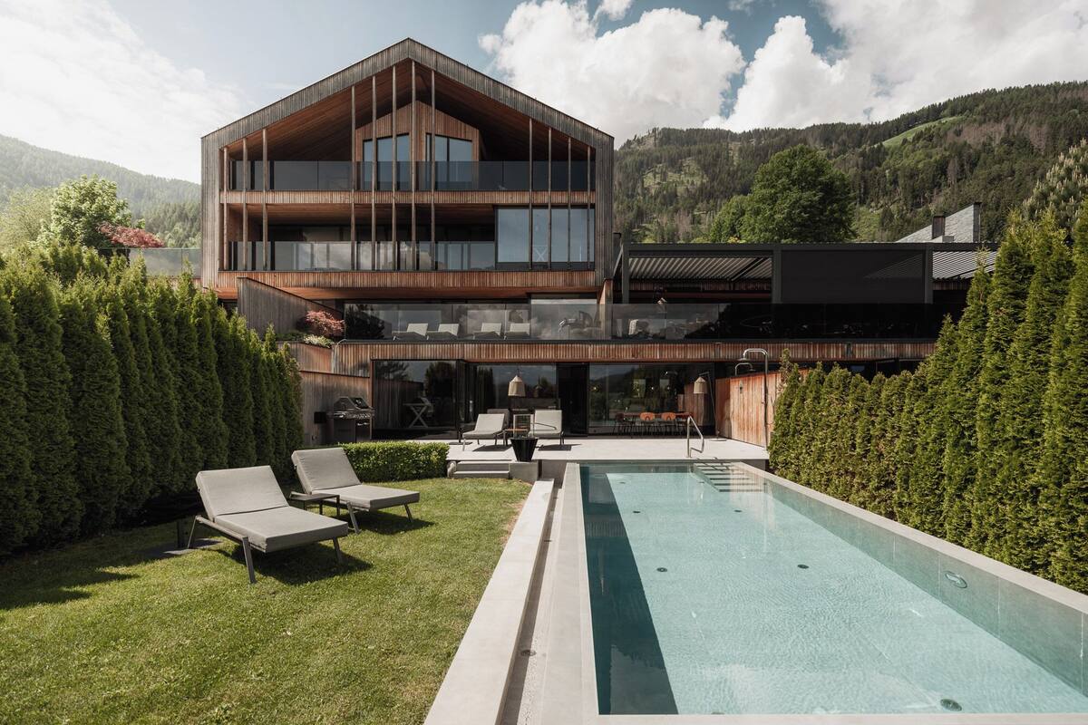 A modern two-story house with a swimming pool, outdoor seating, and a mountainous backdrop.