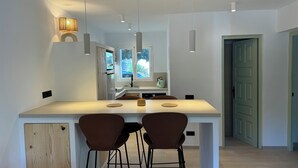 Een moderne keuken met een centraal eiland, twee barkrukken, hanglampen en uitzicht op de buitenlucht via een raam.