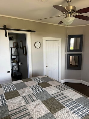 A room with a checkered floor, a ceiling fan, a clock, and a door leading to another room.