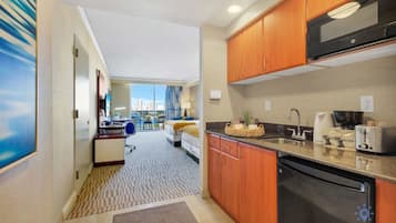 A hotel room with a kitchenette, a dining area, and a view of the cityscape.