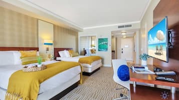A hotel room with two beds, a desk with a computer, a TV, and a view of the beach.